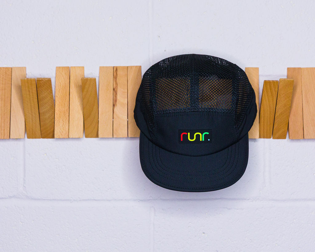 Black mesh technical running hat with curved brim and front Runr logo, hanging on wall.