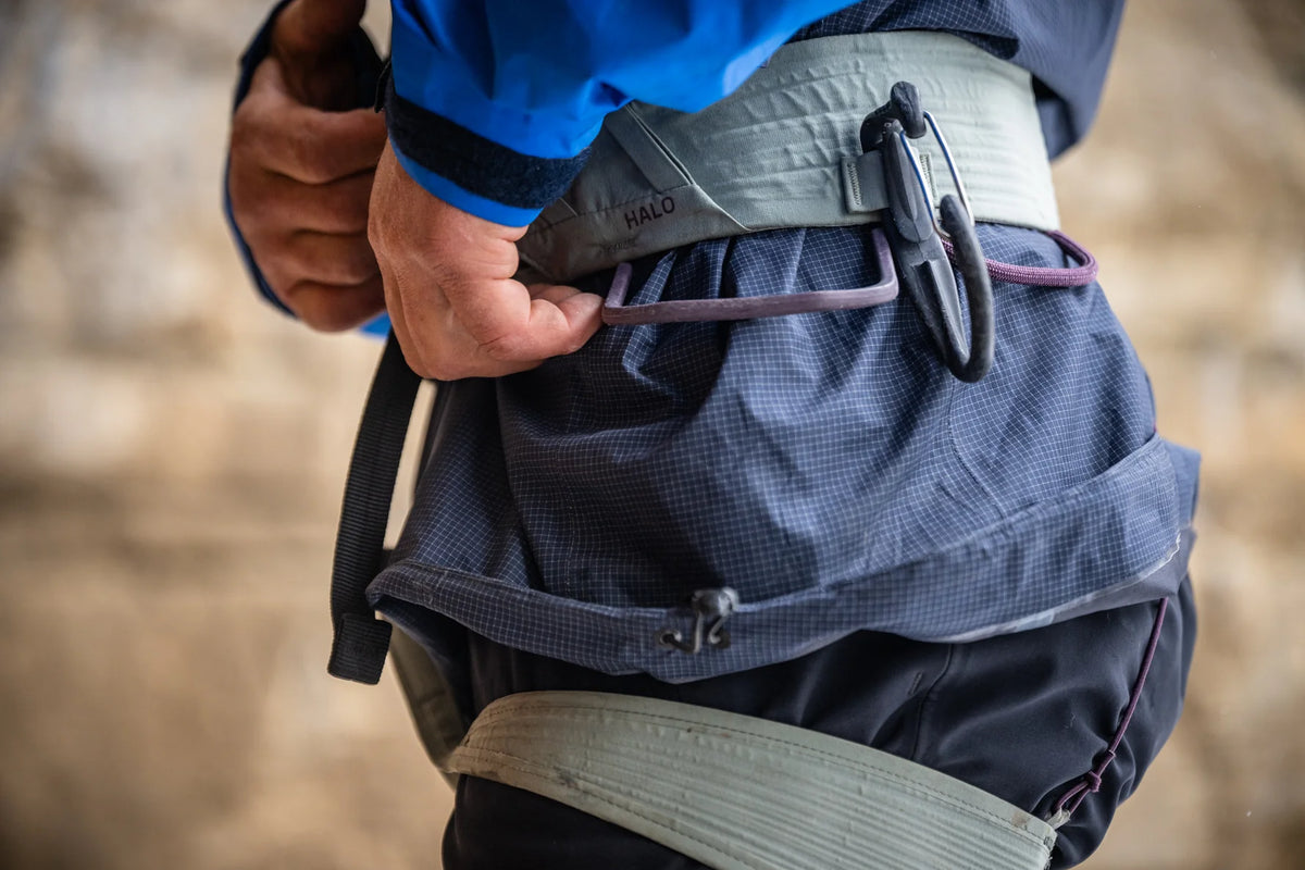 Climbing harness worn at waist with gray padded belt and black adjustment hardware