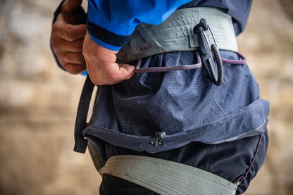 Climbing harness worn at waist with gray padded belt and black adjustment hardware