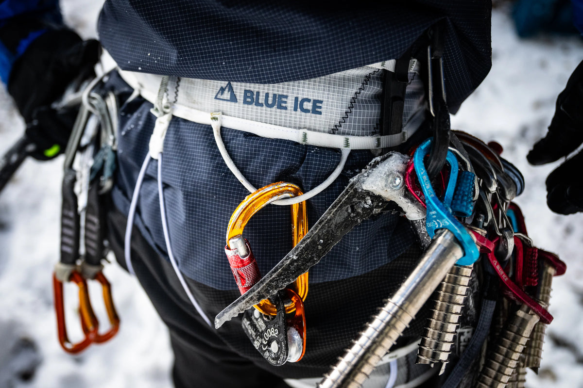 White harness worn with metal carabiners and gear attachments at the belt