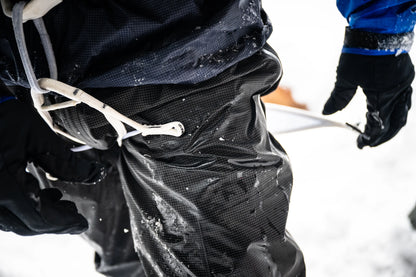 White harness straps on a climber’s dark jacket, with buckles visible near waist