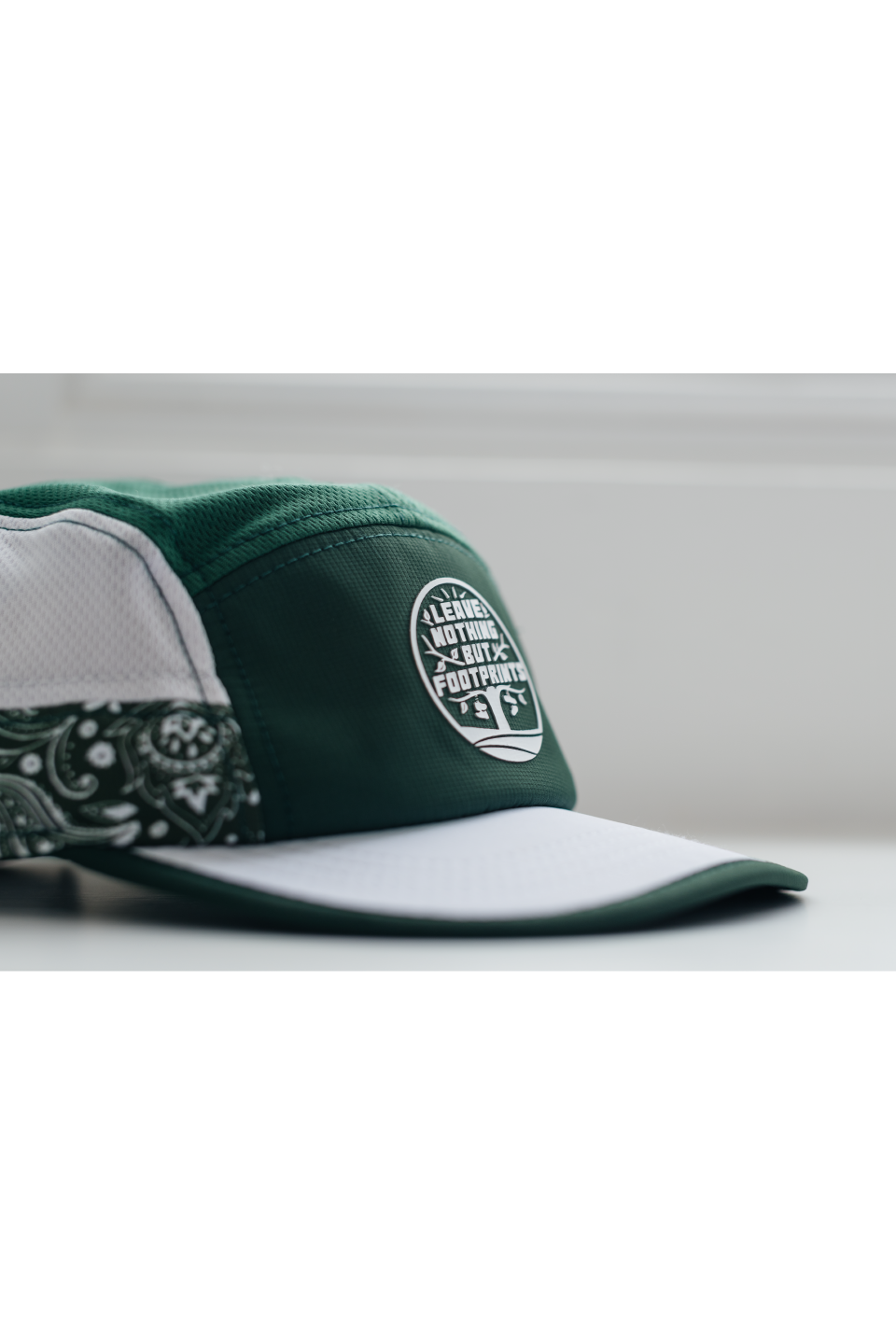 Side view of green running hat with white brim edge and leave-nothing patch logo.