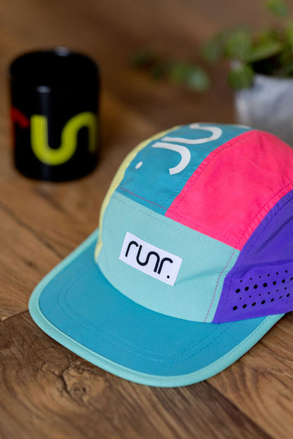 Multicolor technical running hat with front logo patch, teal brim, and side graphics.