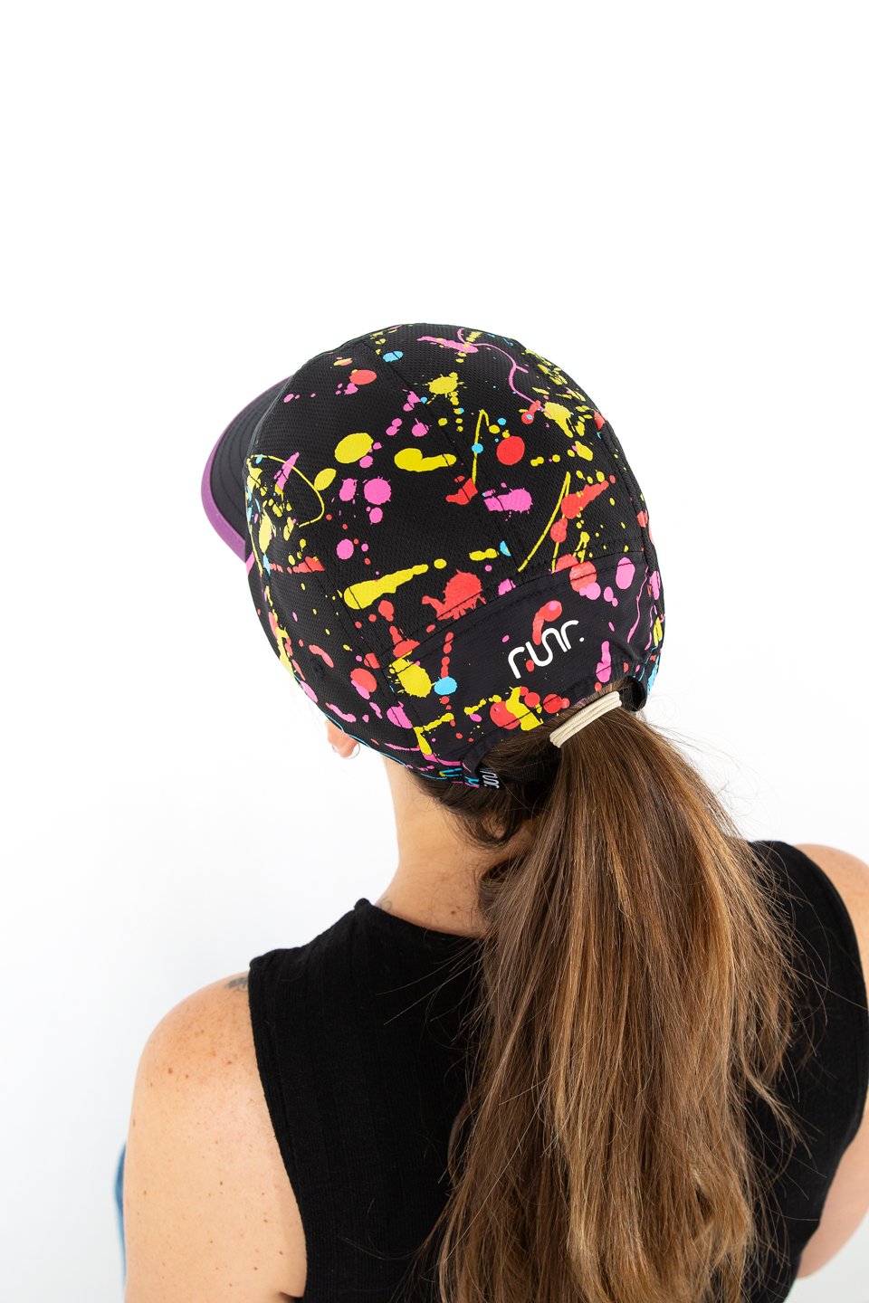 Black technical running hat with multicolor paint-splash print and purple brim, worn from behind.