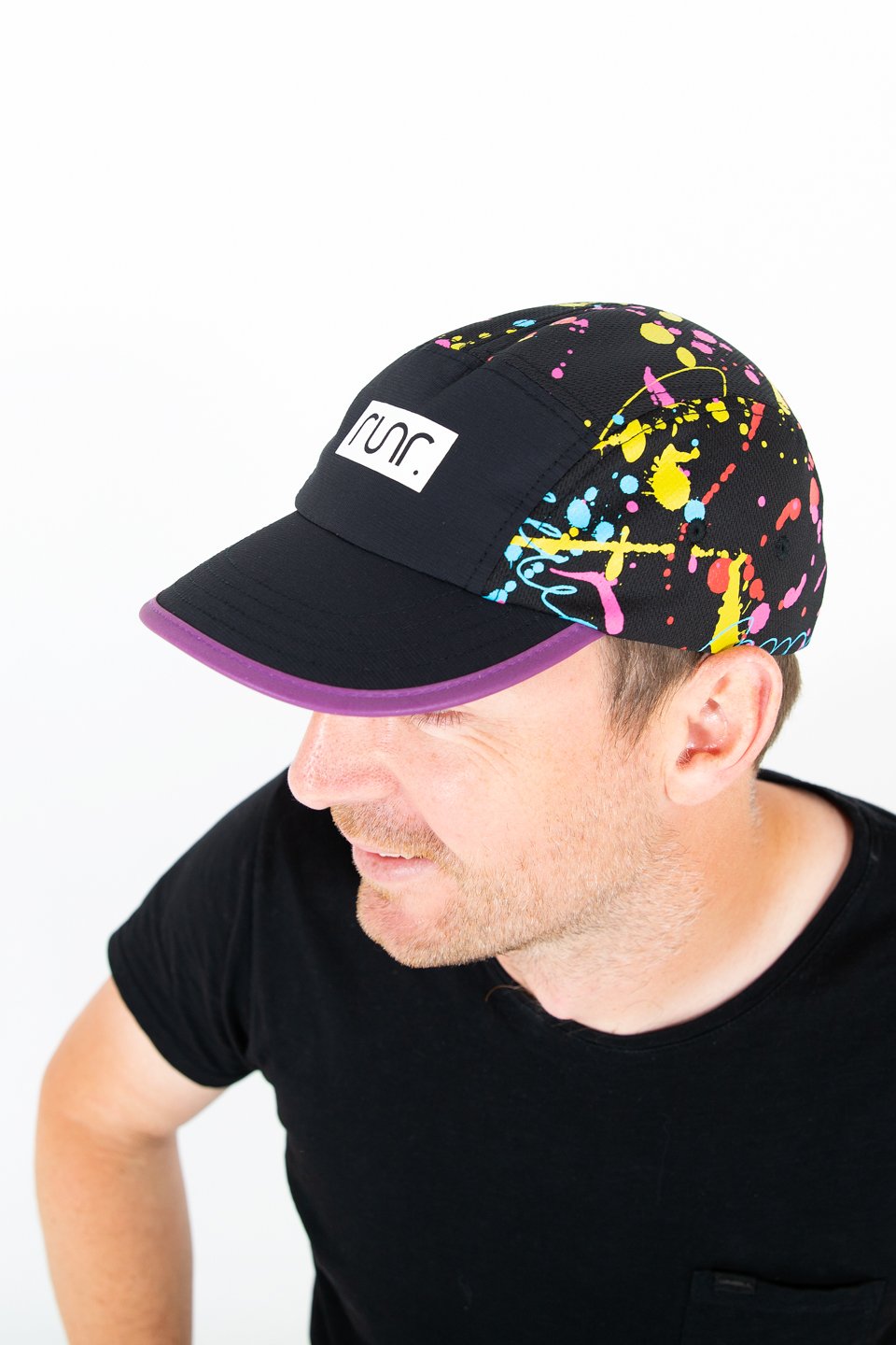 Black technical running hat with multicolor splatter print, purple brim, worn by man.