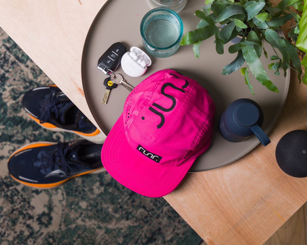 Pink technical running hat resting on a table, showing front RUN logo and brim.