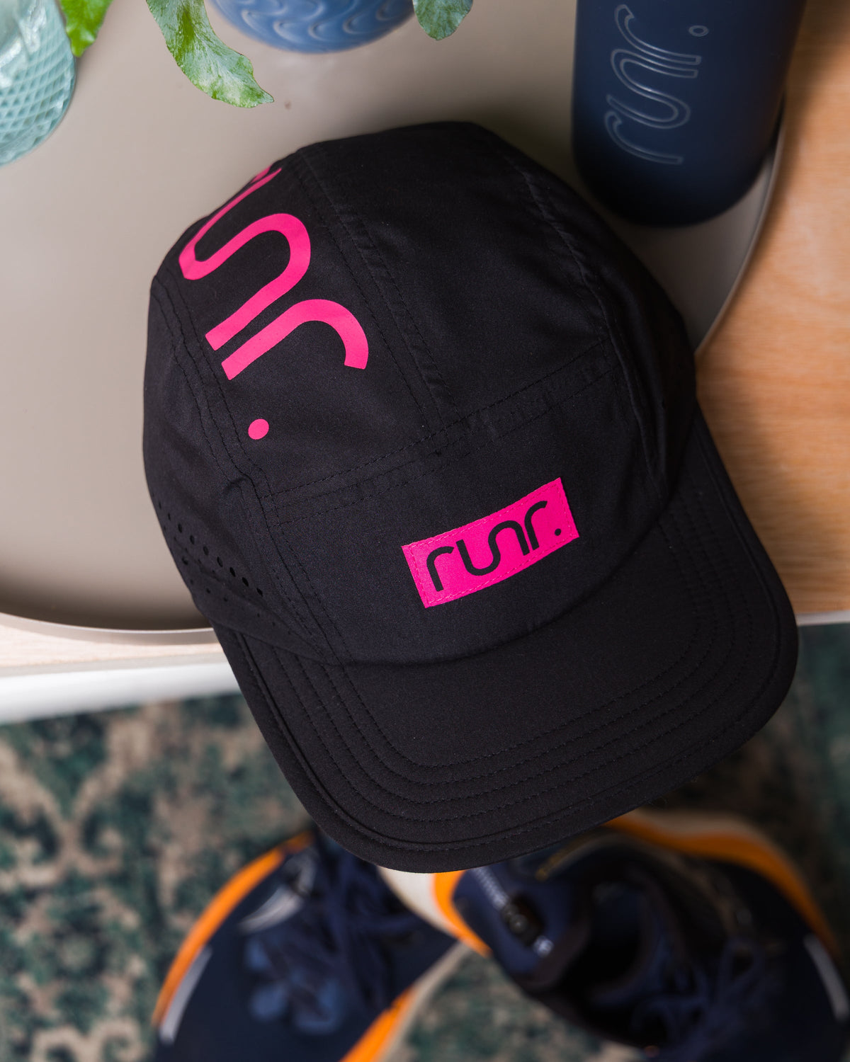 Black running cap close-up with pink side logo and perforated panel stitching.