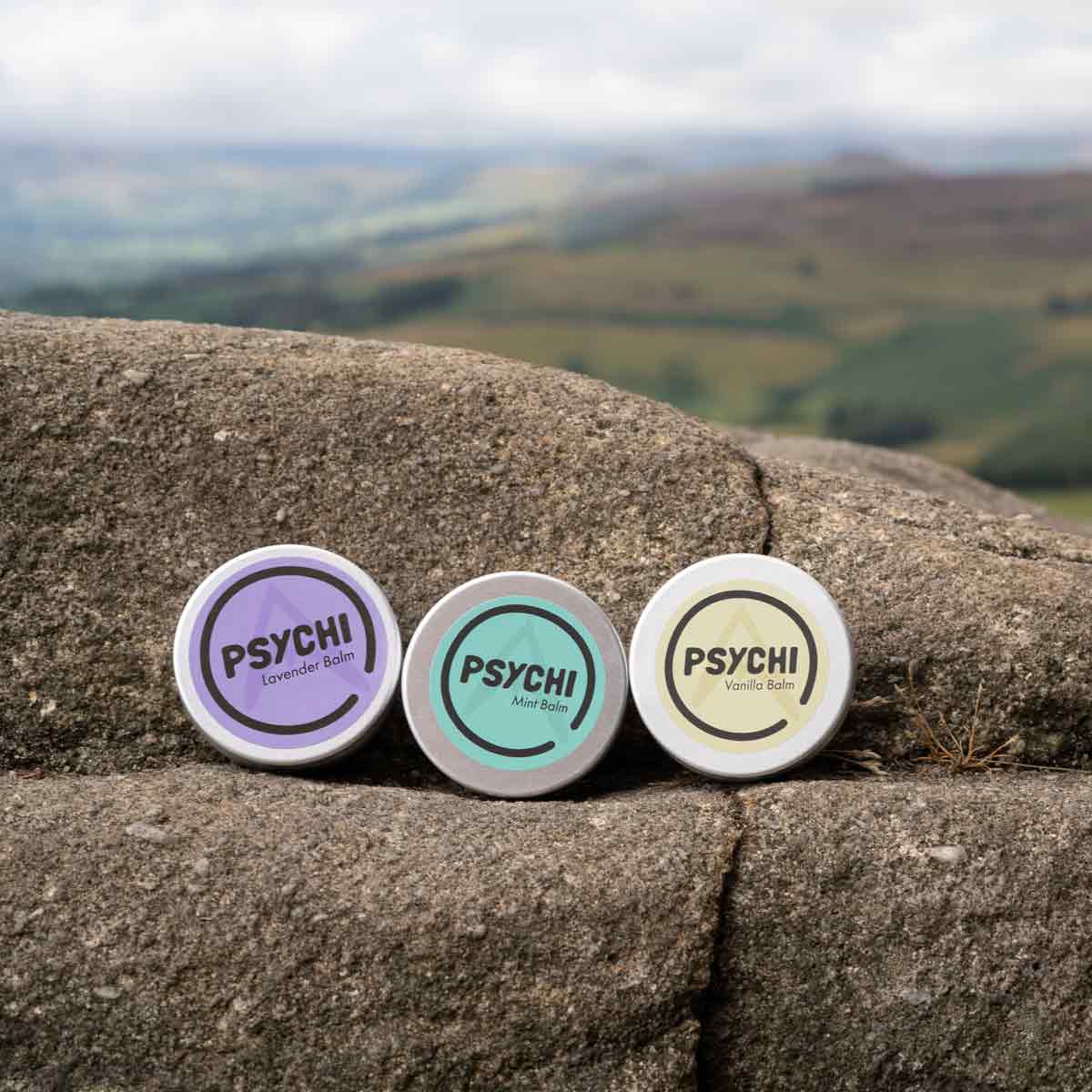 Assorted PSYCHI balm tins on stone: Lavender, Mint, Vanilla