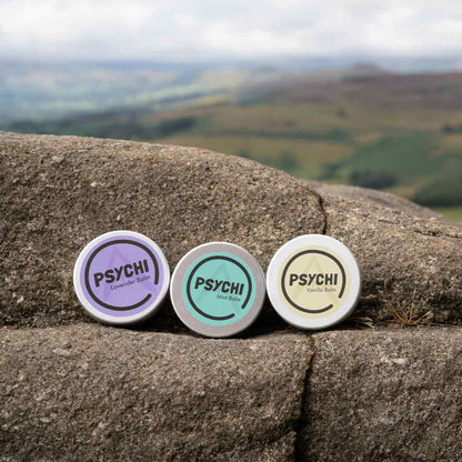 Assorted PSYCHI balm tins on stone: Lavender, Mint, Vanilla