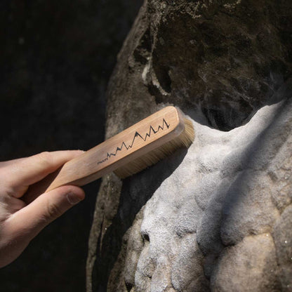 Climbing brush held against rock surface with PSYCHI logo on wooden handle