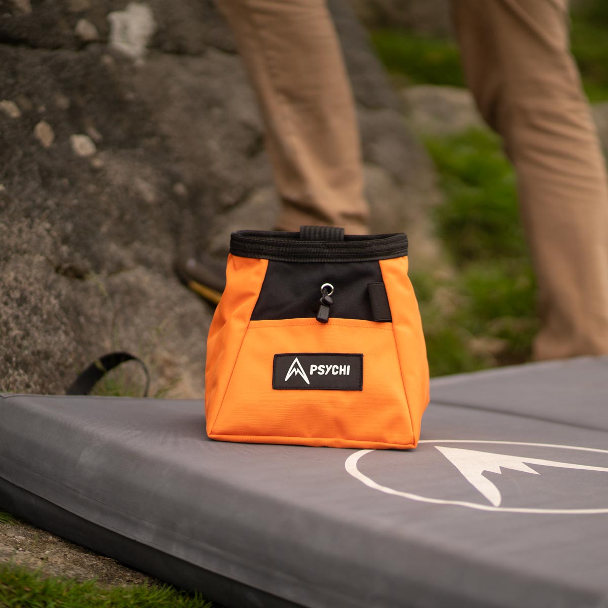 Orange chalk bucket bag with black top strap and PSYCHI patch, on crash pad