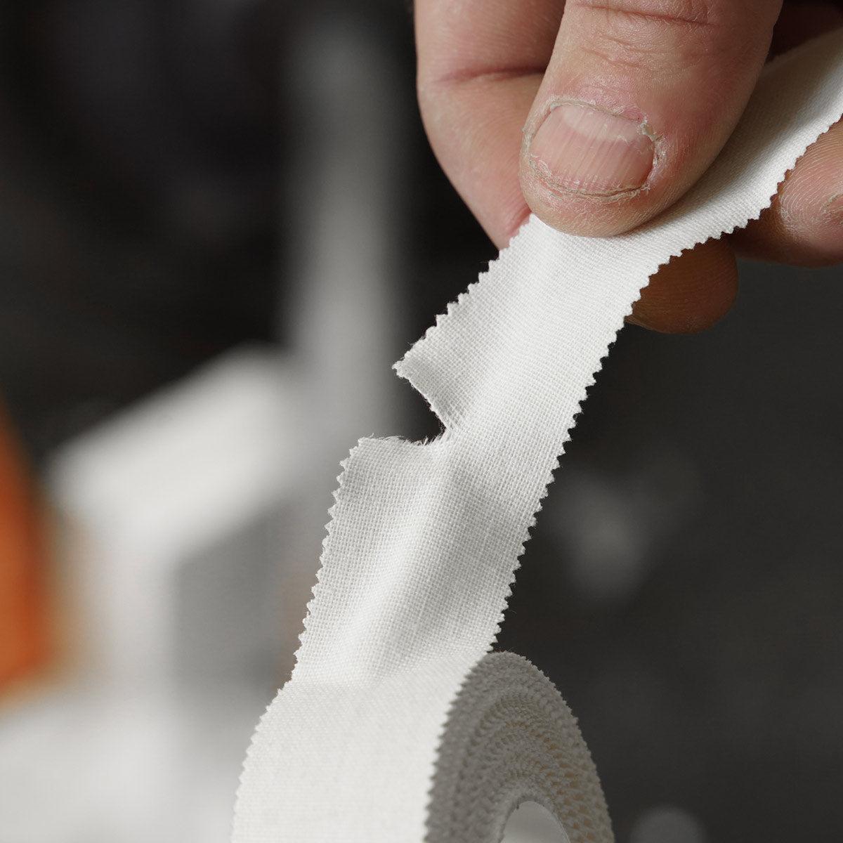 White climbing finger tape strip held by fingers, showing textured fabric edge