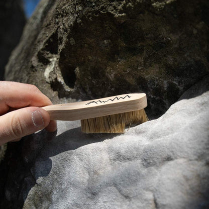 Hand holding boar hair climbing brush with bristles contacting rock