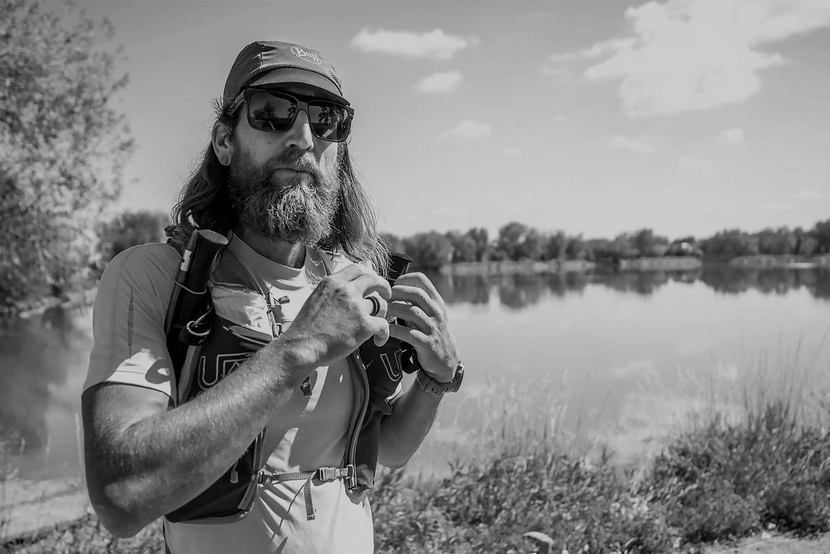Man with a beard and sunglasses holding a camera by a lake, with '2012' text overlay.
