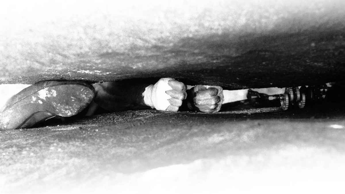 Person climbing a steep ice wall with crampons and ice axes.