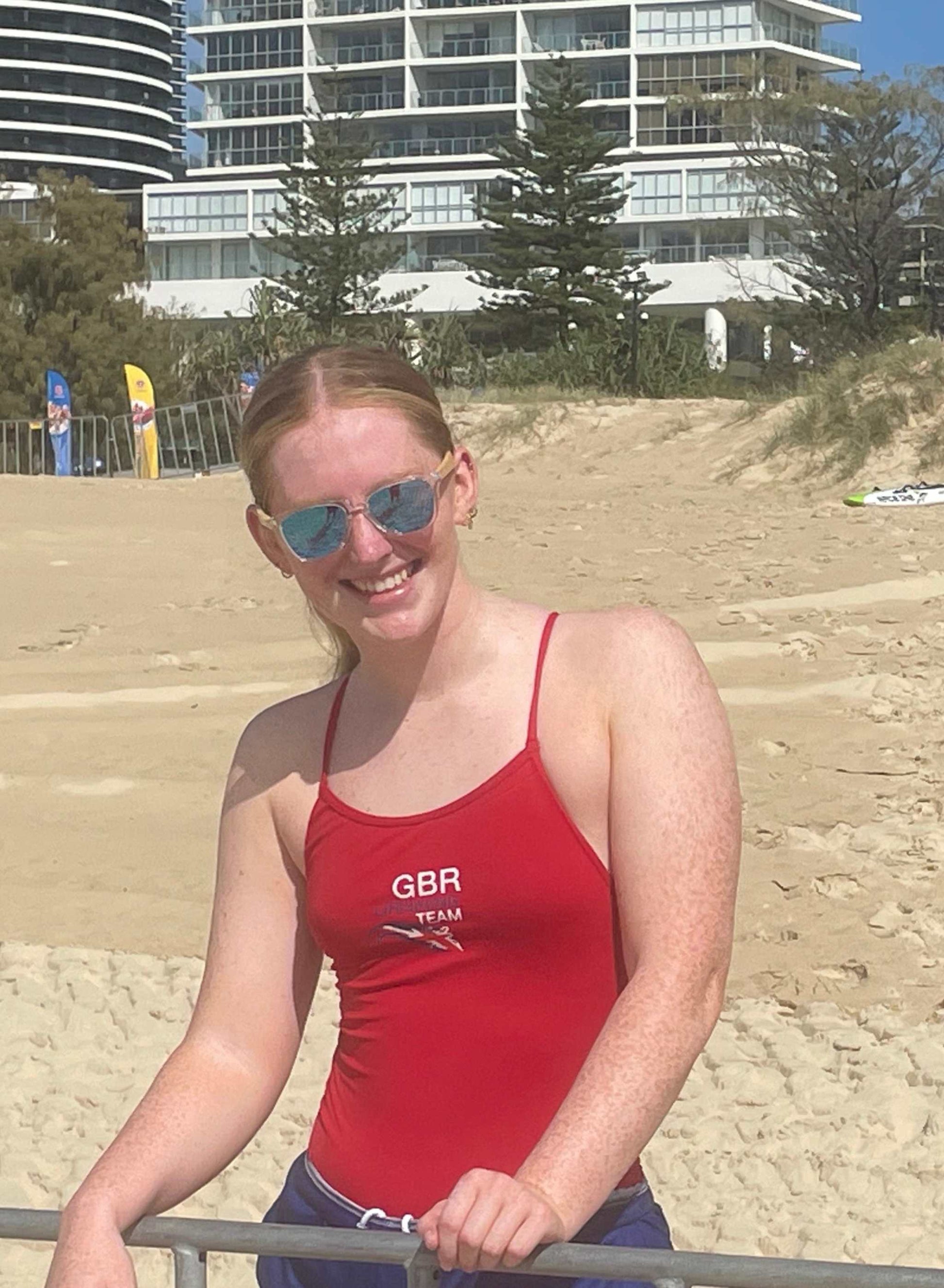 Clear frame sunglasses with pink tinted lenses worn by a person on a sandy beach