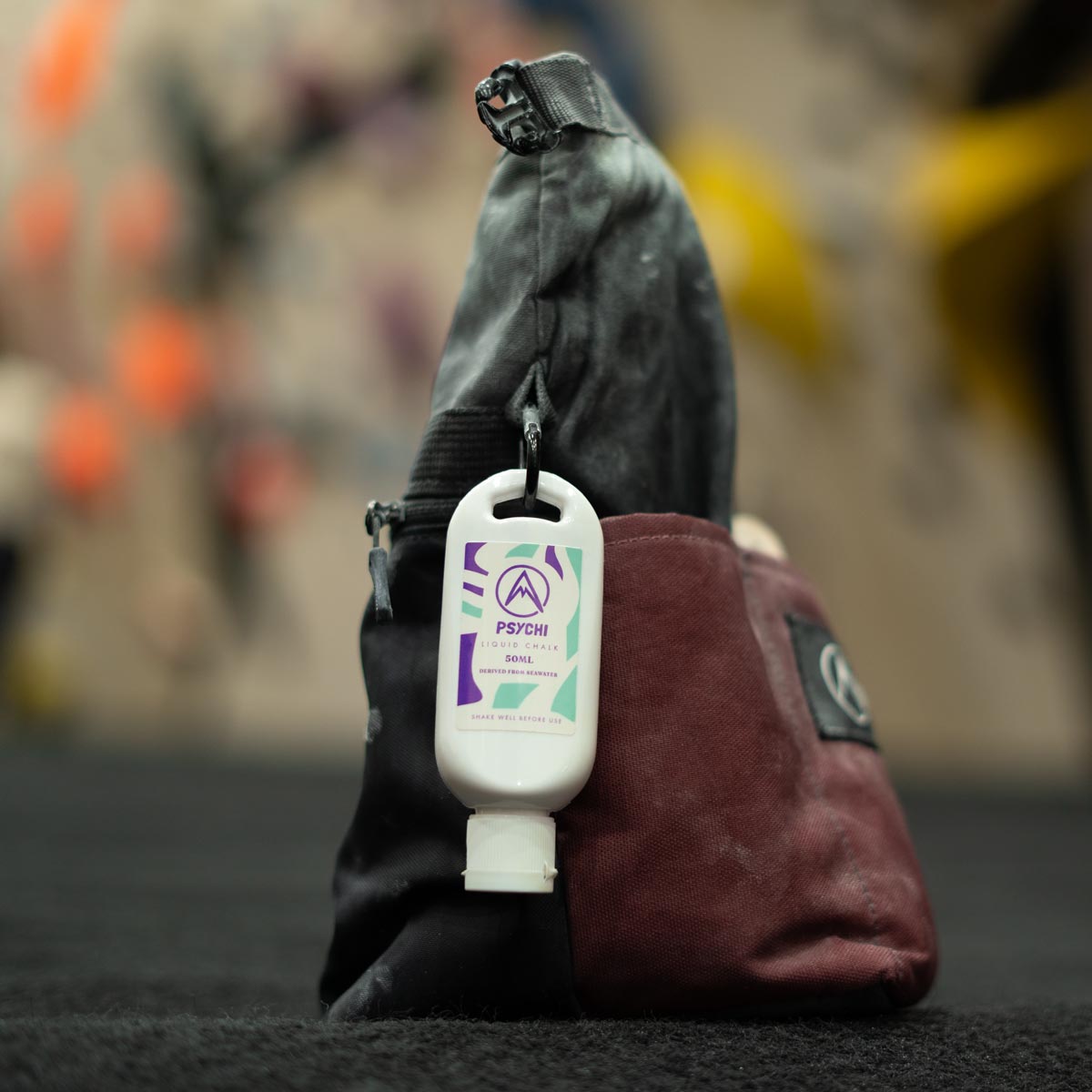 Climbing chalk bottle attached to a bag by a carabiner, white bottle with PSYCHI label