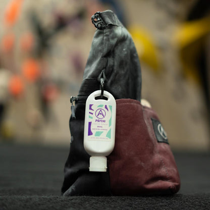Climbing chalk bottle attached to a bag by a carabiner, white bottle with PSYCHI label