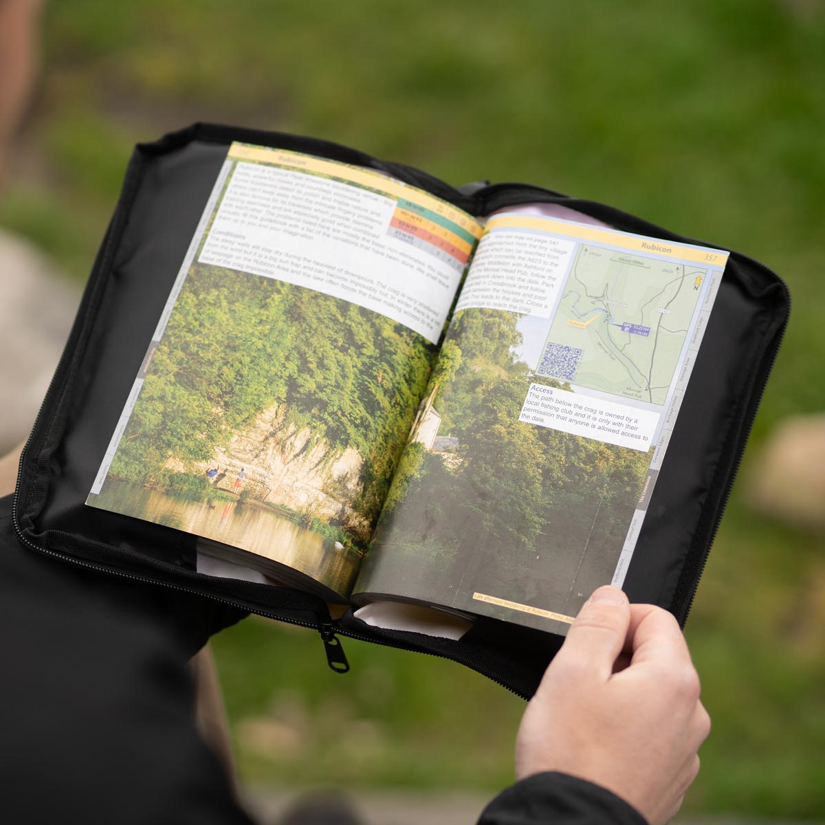 Weatherproof climbing guidebook cover opened, black outer sleeve holding map pages outdoors