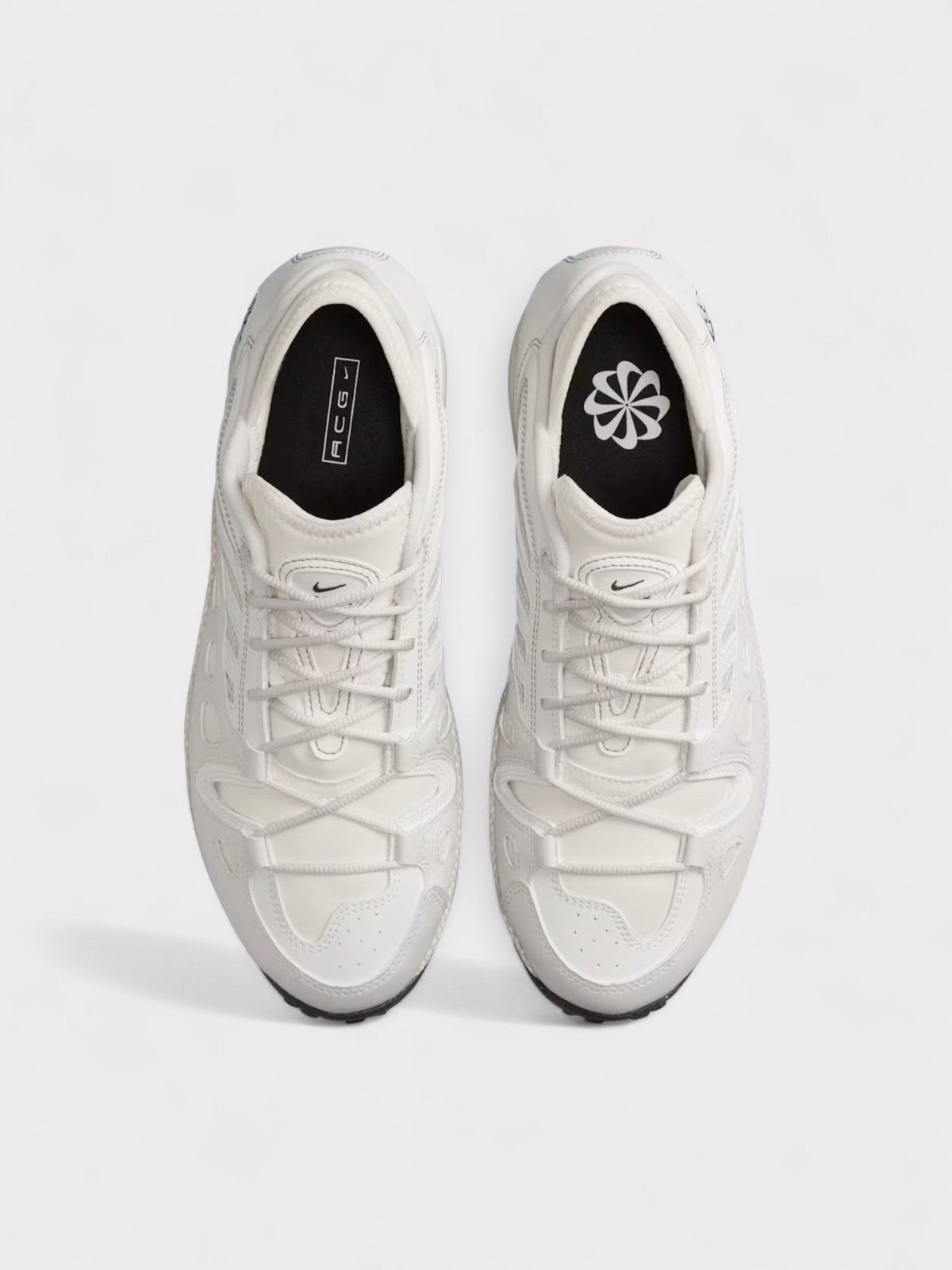 Pair of white lace-up Nike ACG sneakers, toe and tongue with black heel accents