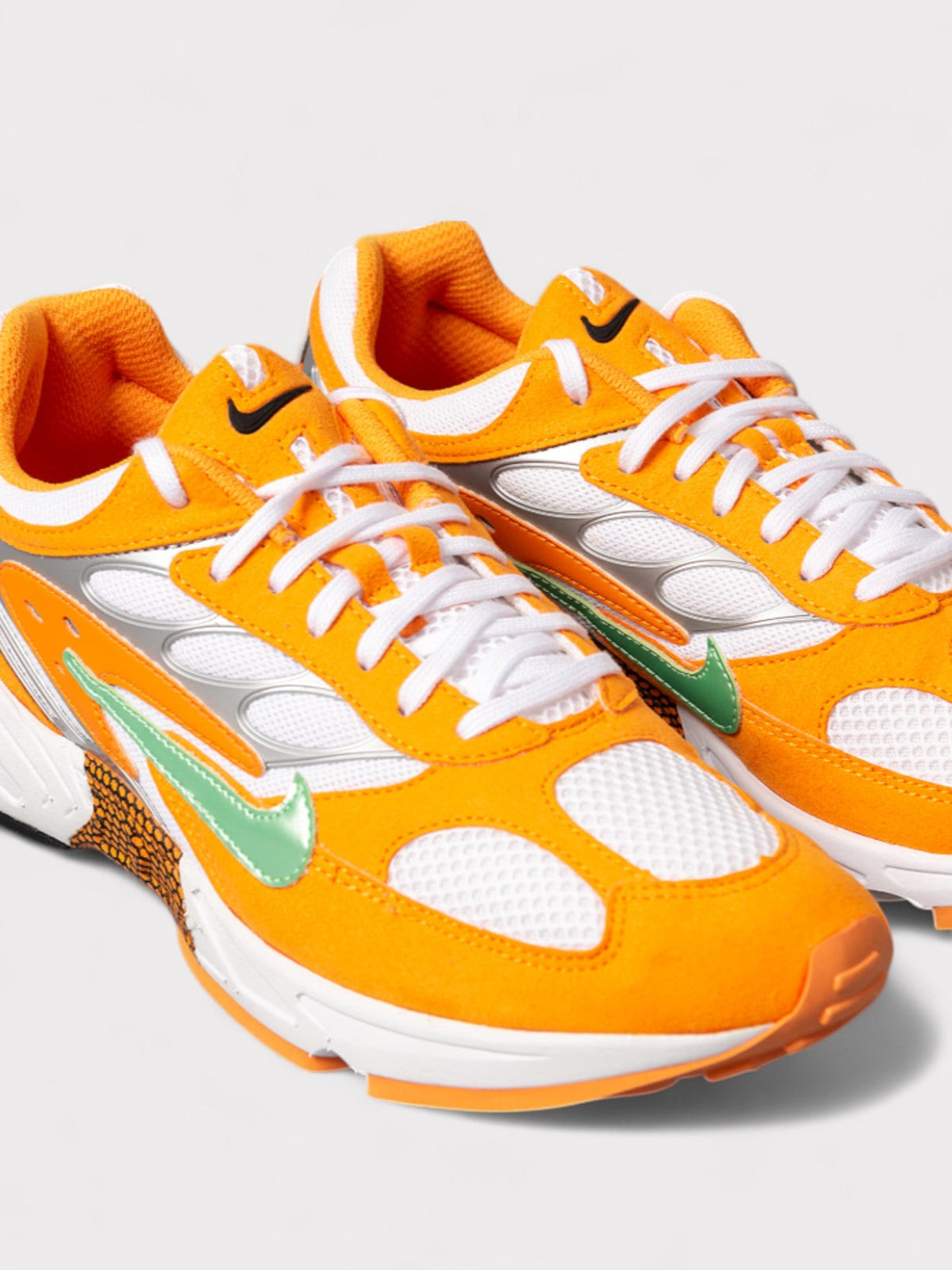 Nike orange and white lace-up sneakers with green swoosh detail, close-up