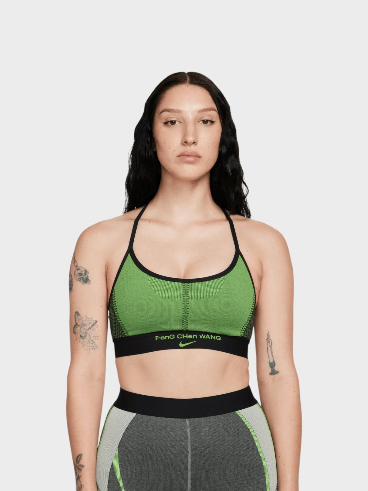 Green sports bra with black trim and thin straps, worn by model