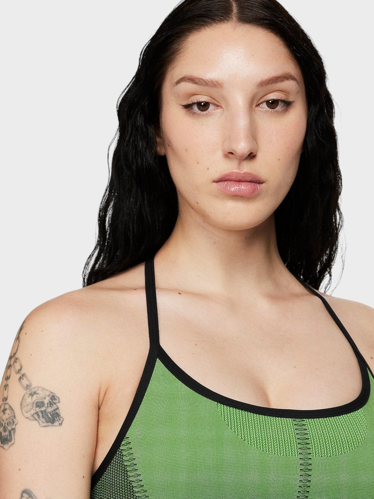 Green sports bra with black trim and thin straps, worn by model