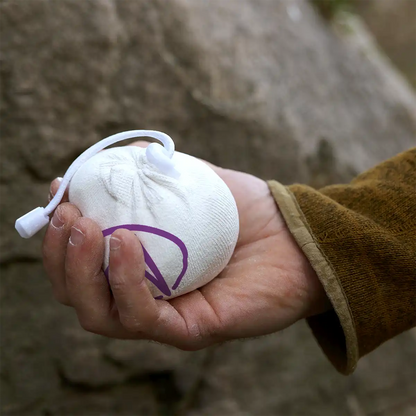 Refillable climbing chalk ball pouch in white with purple logo, held in a hand with cord.