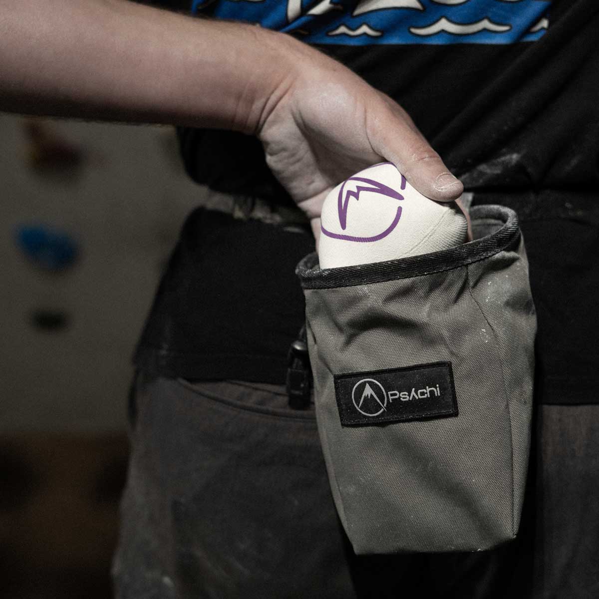 Hand holding white refillable climbing chalk ball pouch with purple logo in a black pouch.