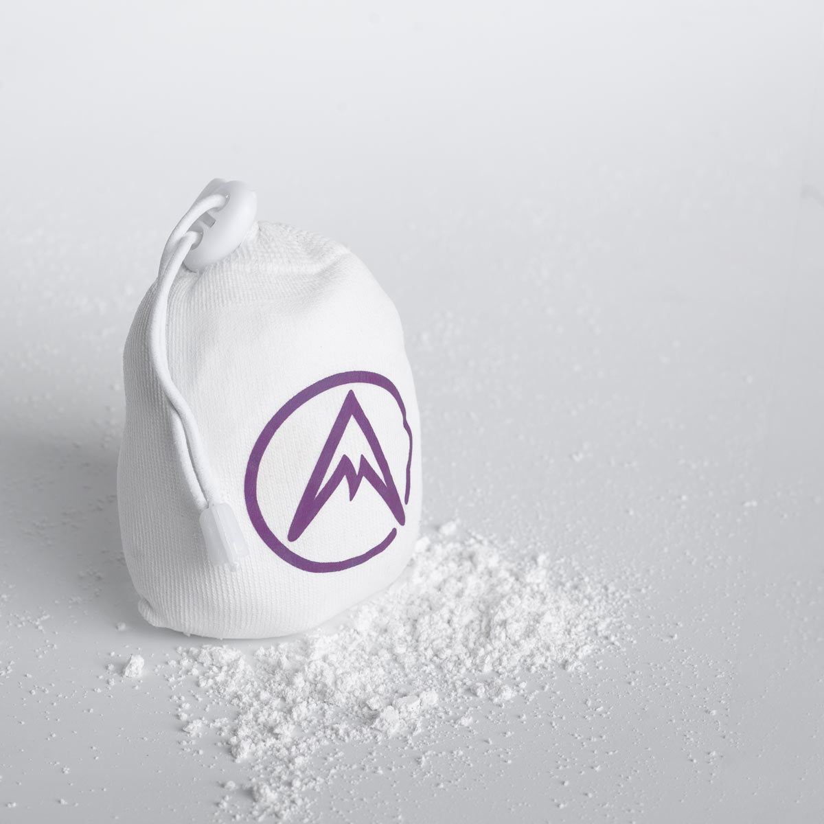 Refillable climbing chalk ball pouch spilling white chalk powder; purple logo and draw cord.