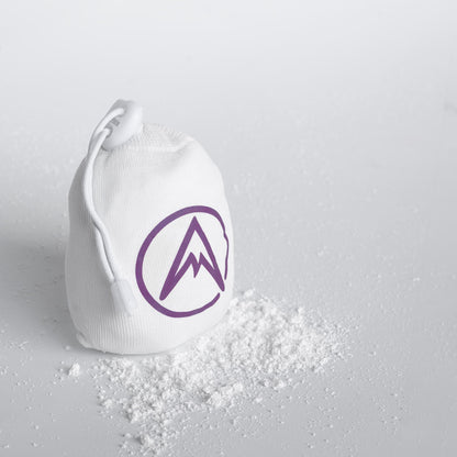 Refillable climbing chalk ball pouch spilling white chalk powder; purple logo and draw cord.