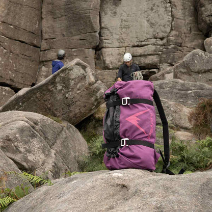 Purple climbing rope bag on rocky trail, worn by helmeted climber