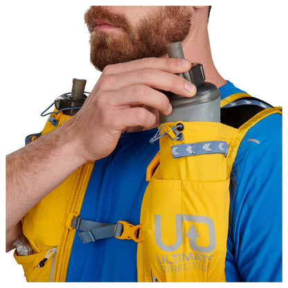 Person adjusting a device on a yellow backpack with 'Ultimate Direction' branding.