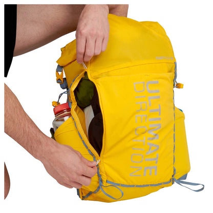 Yellow backpack with 'Ultimate Direction' branding being opened by a person.