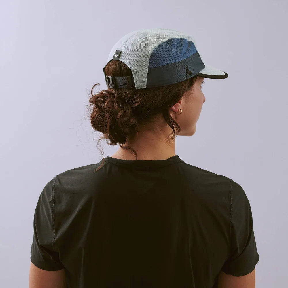 Person wearing a black t-shirt and a white and blue cap on a light gray background