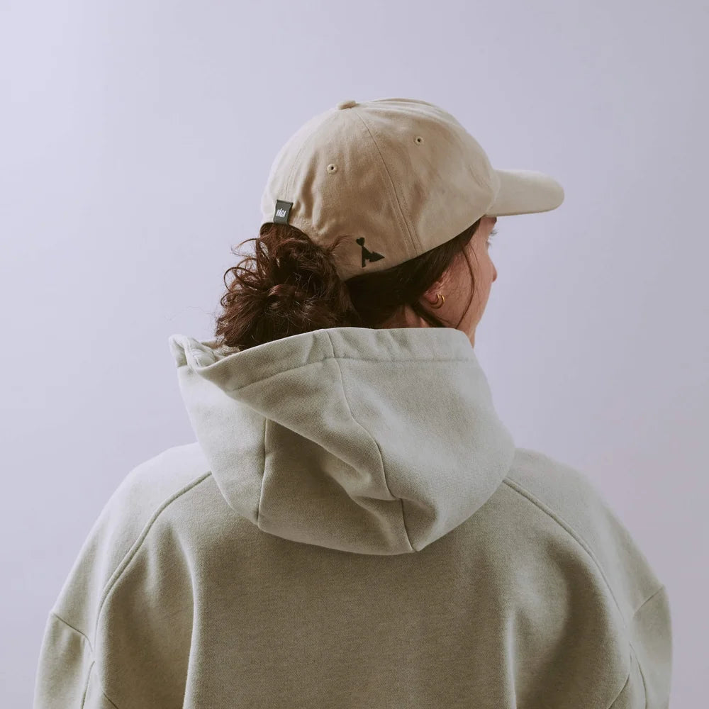 Person wearing a beige cap and hoodie against a light purple background