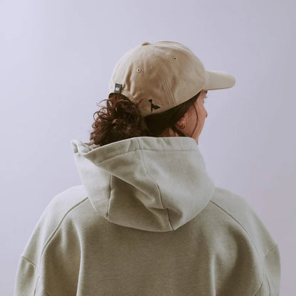 Person wearing a beige cap and hoodie against a light purple background
