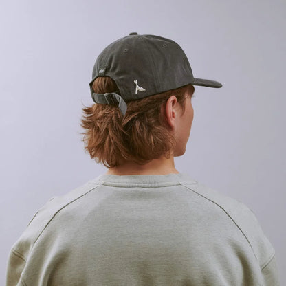 Person wearing a dark gray cap with a small logo on the back, facing away from the camera against a light gray background.