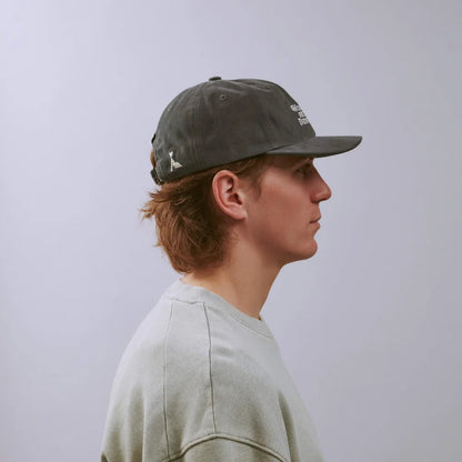 Person wearing a gray cap with a logo on a plain background