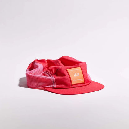 A red flat-brim cap with a mesh back and a rectangular orange patch on the front displaying the brand name 'VAGA'.