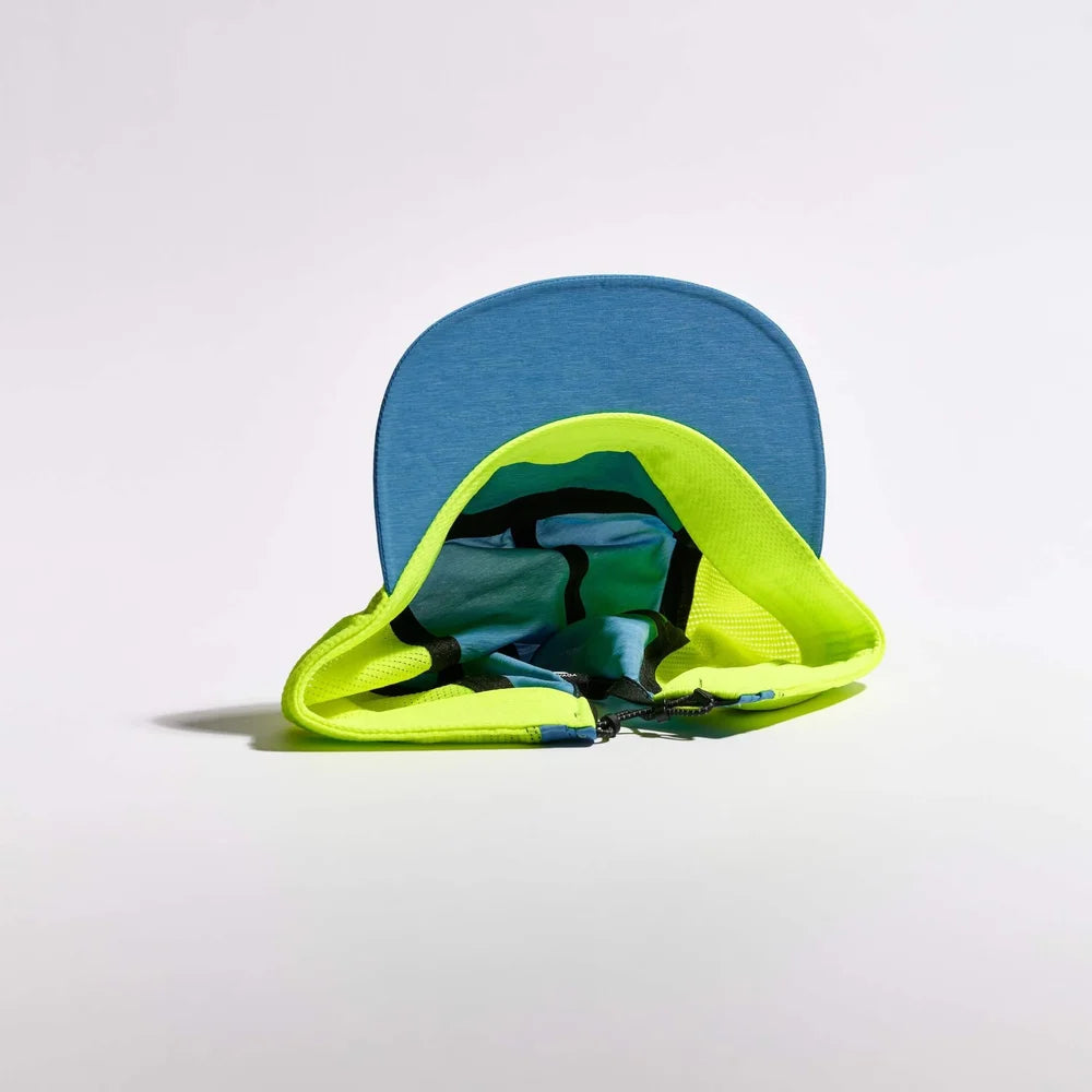 A blue baseball cap with a bright neon yellow-green mesh underbrim and a teal patterned inner lining, photographed on a clean white studio background.